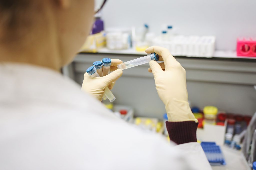 Scientist examining test tubes in a laboratory setting, wearing protective gloves.